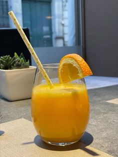 an orange drink in a glass with a straw sticking out of the top, on a table outside