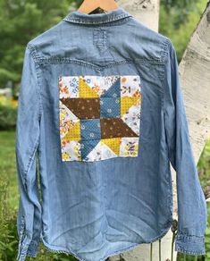 a blue jean jacket with patchwork on the front and back, hanging from a tree