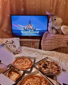 four pizzas are sitting on the table in front of a television with disney's castle on it