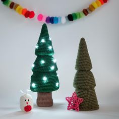 three crocheted christmas trees with lights and a teddy bear next to them on a white background