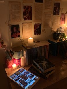 a table topped with lots of books next to a lit candle and some pictures on the wall