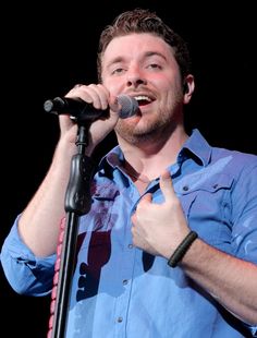 a man singing into a microphone with his hand up in the air while wearing a blue shirt