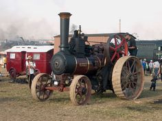 an old steam engine sitting on top of a grass covered field next to other vehicles