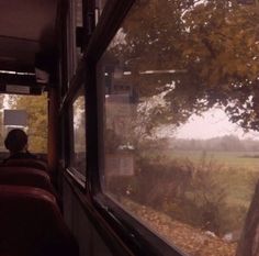 a man sitting on a bus looking out the window at an open field and trees