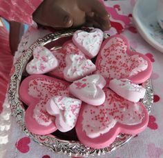 pink and white heart shaped cookies in a bowl on a table with a doll next to it