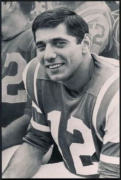 a black and white photo of a football player sitting on the sidelines with other players behind him