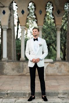 a man in a white tuxedo and black bow tie standing on some steps