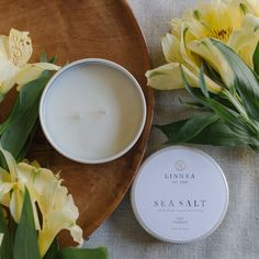 a wooden plate with flowers and a candle on it next to a bowl of sea salt