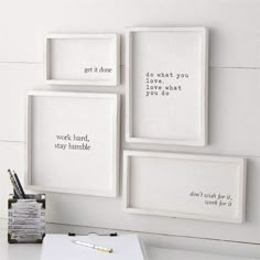 three white framed pictures hanging on the wall above a desk with a pen and pencil