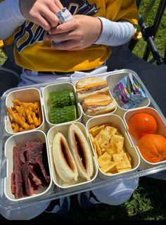 a person sitting down holding a tray with food in it and an orange on the side