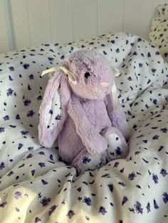 a purple stuffed animal sitting on top of a bed covered in white and blue sheets