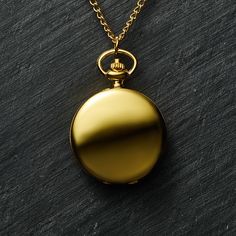 a gold colored pocket watch on a black surface with a golden chain around the neck