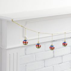 christmas ornaments hanging from a string in front of a brick fireplace with white paint and gold trim