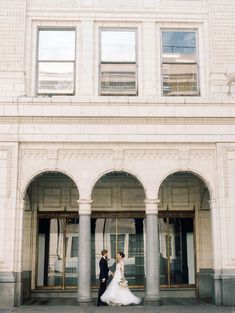 a bride and groom walking in front of a building