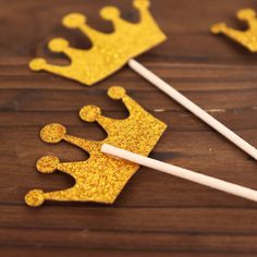 two straws with gold glittered crowns on them sitting next to toothpicks