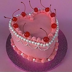 a heart shaped cake with cherries and pearls on the top is sitting on a purple plate