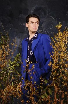 a man in a blue suit standing next to some plants