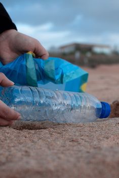 a person picking up a plastic bottle from the sand