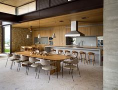 an open kitchen and dining room area with large wooden table, bar stools and chairs