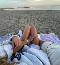 a woman laying on top of a beach covered in a blanket next to the ocean