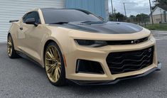 a tan chevrolet camaro with gold rims parked in front of a garage door