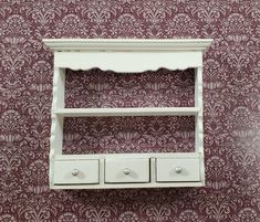 a white shelf with three drawers against a red wallpapered background in a room