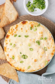 a pizza with cheese and green onions in a bowl next to crackers on a plate