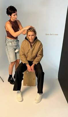 a woman is sitting on a stool while a man stands behind her and combs his hair