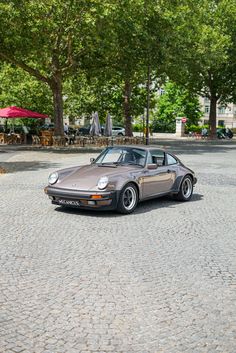 a car parked on the street in front of some trees and tables with umbrellas