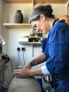 a woman in blue shirt working on a pottery pot with hands and feet resting on it