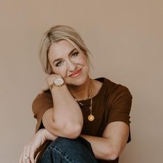 a woman sitting on the floor with her hand under her chin and looking at the camera