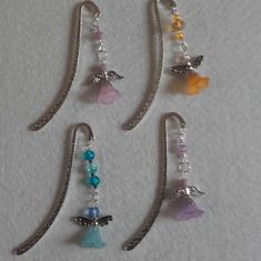 four pairs of dangling earrings with beads and charms attached to them on a white surface