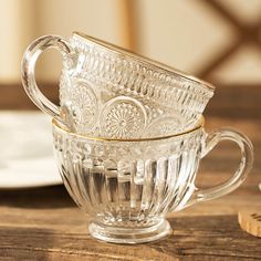 two clear glass cups sitting on top of a wooden table next to a white plate