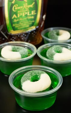 four green jello cups with powdered sugar in them and a bottle of apple cider