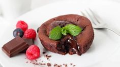 a piece of chocolate cake on a plate with raspberries and mint next to it