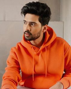 a man in an orange hoodie sitting at a table with his hands on his hips