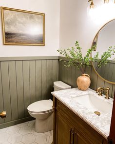 a white toilet sitting next to a sink in a bathroom under a framed painting on the wall