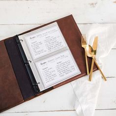 an open menu book sitting on top of a wooden table next to utensils