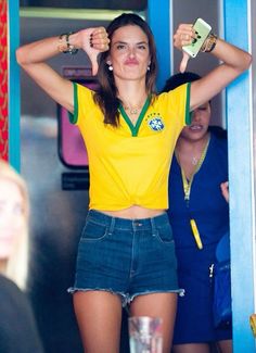 a woman in a yellow shirt and jean shorts is holding her hands behind her head