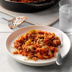 a white plate topped with food next to a glass of water and a skillet