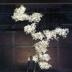 a man standing in front of a sculpture made out of paper flowers and chains hanging from the ceiling