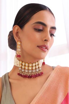 Gold toned choker necklace with kundan and red stones embellishments. Comes with a matching pair of earrings.
Components: 1 Necklace, Pair of earrings
Type: Kundan, Stones
Composition: Brass
Color: Red
Other Details: 
Handmade
Dimensions L x W (in inches):
Necklace: 8.6 x 2.5
Earrings: 2.5 x 0.6
Product Weight (in gms): 350
Closure:
Necklace: Pull-out cord
Earrings: Push back clasp - Aza Fashions Red Kundan Temple Necklace With Stone Work, Red Ruby Kundan Necklace For Diwali, Red Kundan Temple Necklace, Red Ruby Chandbali Kundan Necklace, Heavy Red Kundan Temple Necklace, Red Kundan Jewelry With Cutdana, Red Kundan Necklace With Cutdana In Temple Jewelry Style, Red Kundan Necklace With Cutdana In Temple Style, Red Jewelry Sets For Celebration