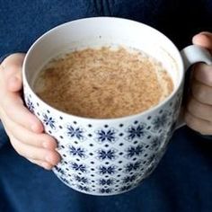 a person is holding a coffee mug with cereal in it and their hands are on the cup