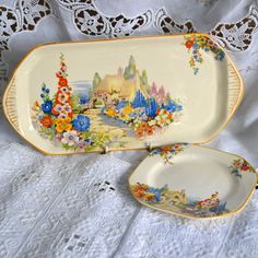 two porcelain dishes sitting on top of a white doily covered tablecloth next to each other