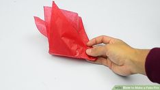 someone is holding an origami piece of red paper with one hand on it