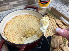 someone is dipping cheese on top of crackers in a red pot with other snacks