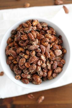 a white bowl filled with nuts sitting on top of a wooden table next to a napkin