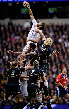 a group of men playing rugby against each other in front of an audience at a stadium