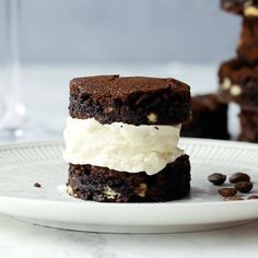 three chocolate brownies with ice cream and coffee beans on a white plate next to two glasses