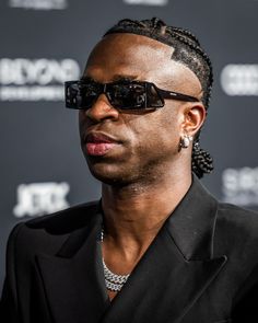 a man wearing sunglasses and a black suit looks off to the side while standing in front of a red carpet